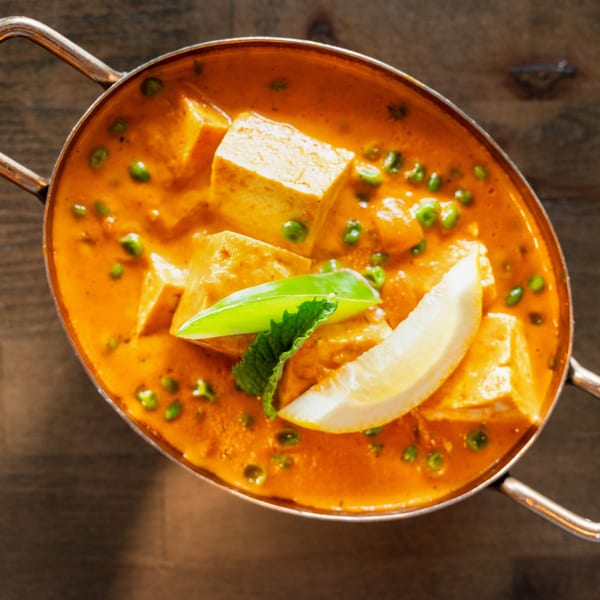 Mutter Paneer in a copper karahi, garnished with a lemon wedge and mint leaves.
