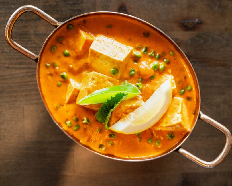 Mutter Paneer in a copper karahi, garnished with a lemon wedge and mint leaves.