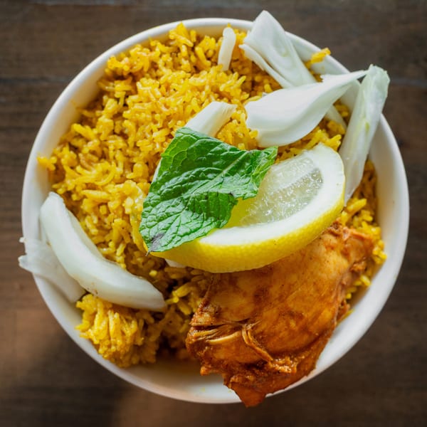 Overhead view of chicken biryani with lemon, mint, and sliced onions in a white bowl.