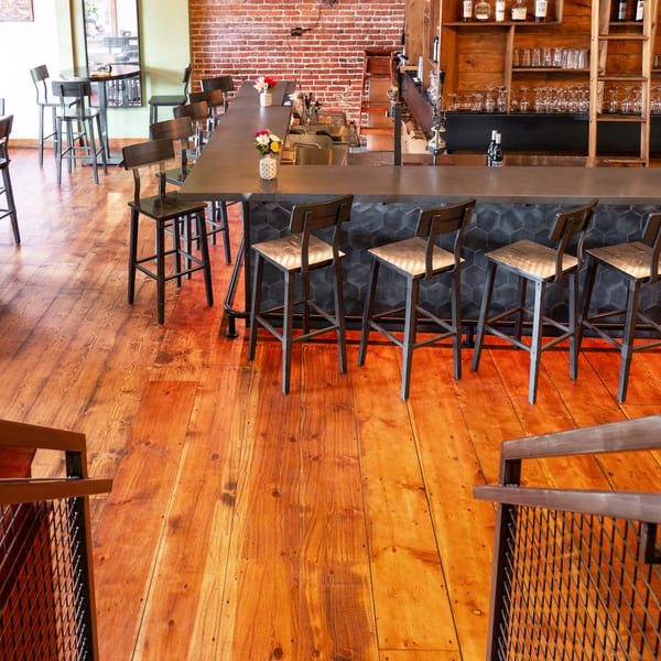 A rustic bar area with a long counter, bar stools, and wooden floors.