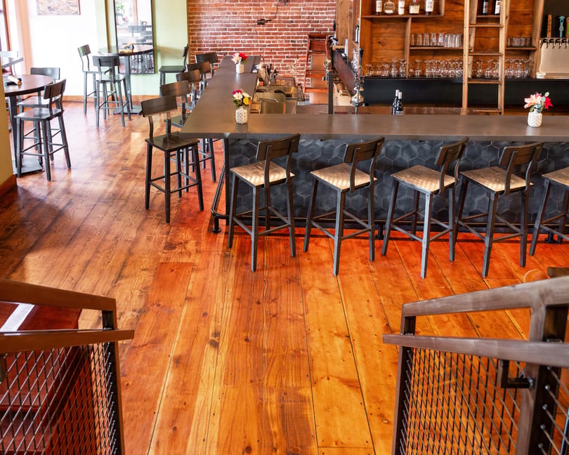 A rustic bar area with a long counter, bar stools, and wooden floors.