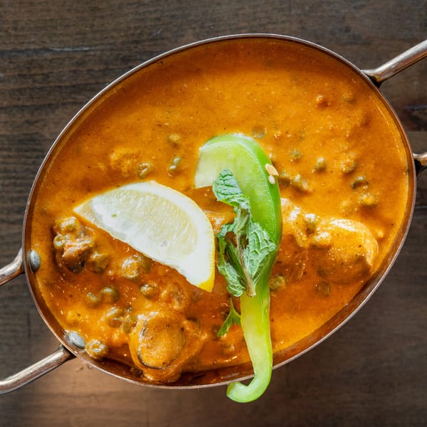 Overhead view of a copper pot filled with orange curry, garnished with lemon, mint, and chili.