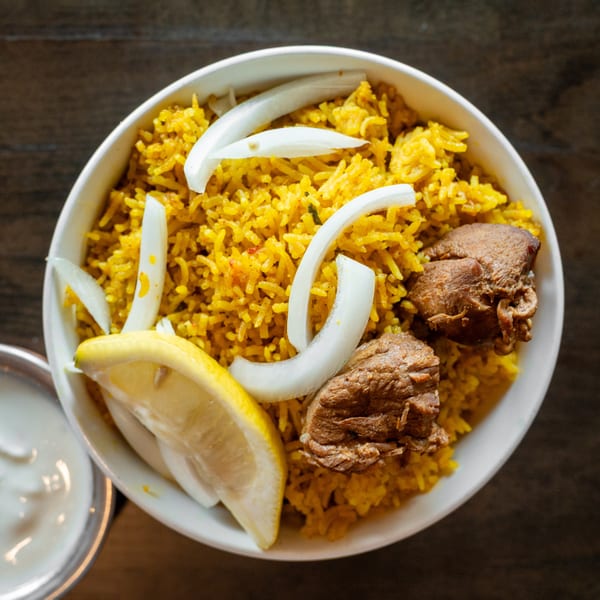 Overhead view of a bowl of yellow rice with meat, onion slices, and a lemon wedge.