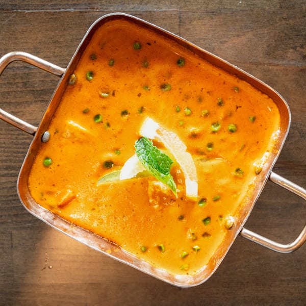 Overhead view of a square copper pot filled with orange curry, peas, and garnished with mint and lime.