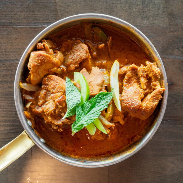 Chicken curry in a metal pot, garnished with mint leaves, lime, and lemon slices.