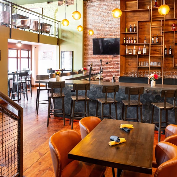 A restaurant interior with a bar, high-top tables, and a mezzanine level with additional seating.