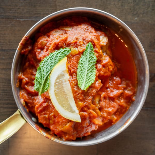 Chicken tikka masala in a copper pot, garnished with a lemon slice and mint leaves.