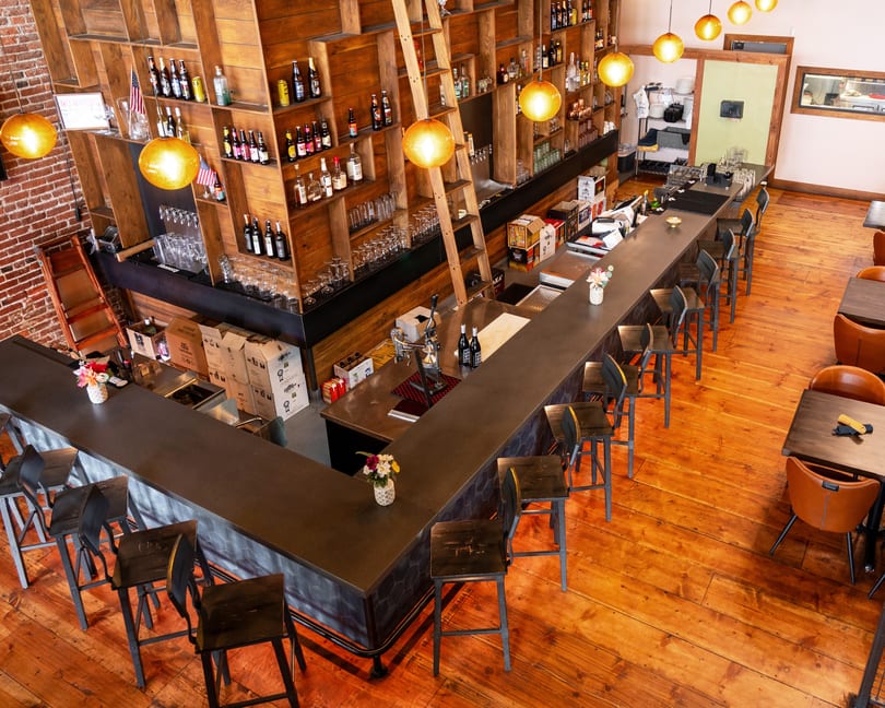 Overhead view of a restaurant bar with wooden shelves, bar stools, and dining tables.