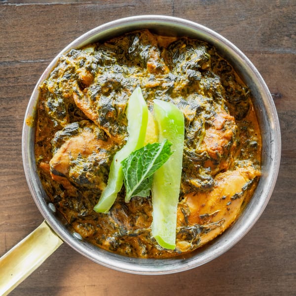 Chicken saag in a metal pan with a brass handle, garnished with lime and mint.
